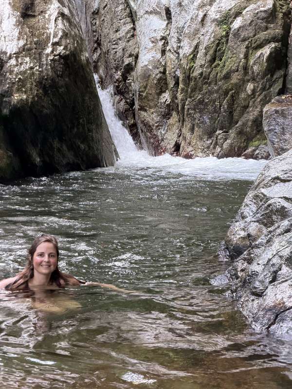 Sarah schwimmt im Naturpool unter dem Wasserfall